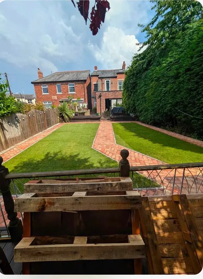 Long back garden with lawn, brick edging and a timber planter by a Victorian house