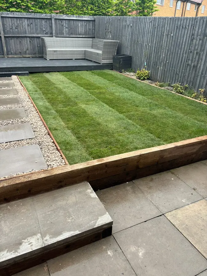 Striped fresh turf beside sleeper edging and a grey patio
