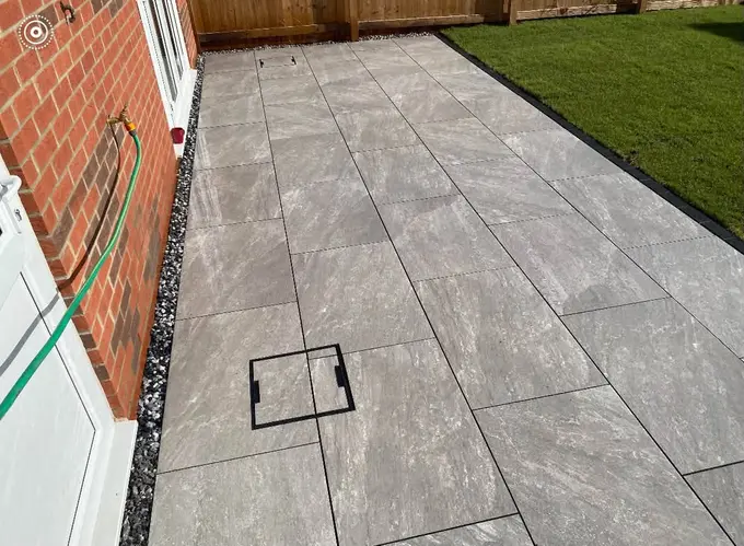 Grey porcelain patio laid along the back of a red brick house beside a lawn