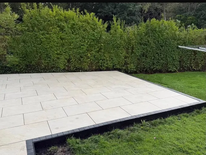 Light porcelain patio with dark edge border set into a lawn